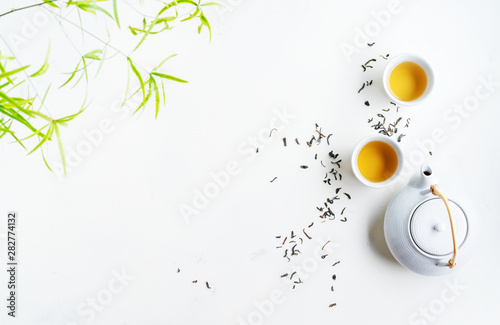 Asian tea concept, two white cups of tea and teapot surrounded with dry green tea  leaves , space for a text on white background. Brewing and Drinking tea.