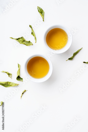 Asian tea concept, two white cups of tea and teapot surrounded with dry green tea  leaves , space for a text on white background. Brewing and Drinking tea.