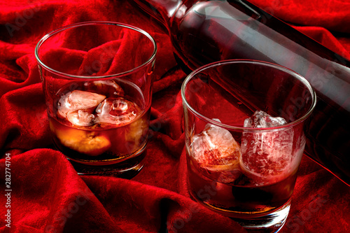 Alcoholism and nightcap drink concept theme with close up on an expensive bottle of single malt scotch and two glasses of whiskey on the rocks on red velvet background