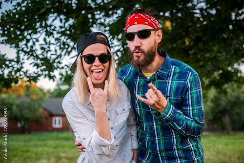 Funny man, woman with protruding tongues in rocker style scream. Family of fun hipsters fooling around outdoors in nature