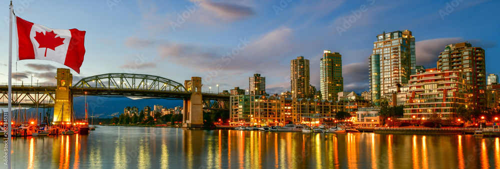 Fototapeta premium Kanadyjska flaga przed widokiem Wyspa Granville w pobliżu Burrard Street Bridge o zmierzchu w Vancouver, Kanada