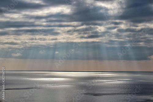 The sun s rays penetrate through the clouds. The sun over the sea. Sun glare on the water.