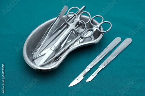 Basic surgical instrument forceps tweezers scissors in emesis or plus basin and scalpel on surgical green drape fabric