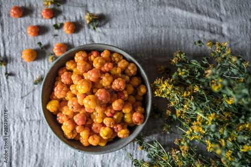 A bowl of cloudberry and dried Hypericum on the table. Background gray linen.