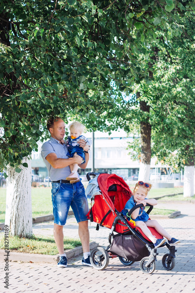 Obraz premium father walks with children, stroller, summer, caucasian family