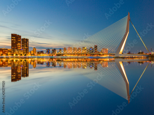 The Erasmusbrug and the Rotterdam skyline by night with a reflection in the water, a famous landmark in the Netherlands and travel destination photo