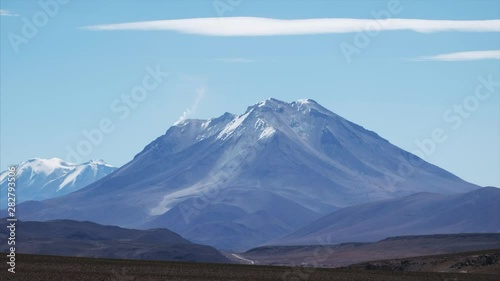 Snow capped mountains of Bolivian Altiplano with smoking volcano photo