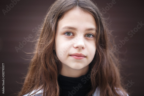 close-up portrait of little beautiful stylish kid girl with long flowing hair against a brown striped wall