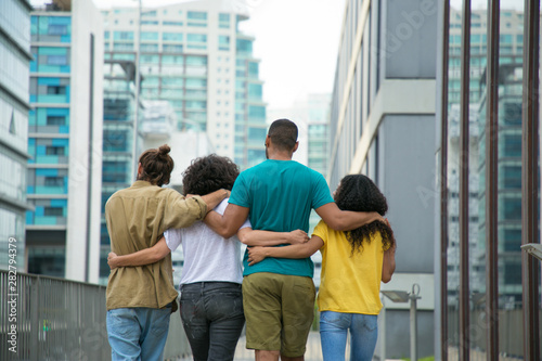 Close male and female friends walking down city street together. Rear view of mix raced people walking outside and hugging each other. Friendship and support concept photo