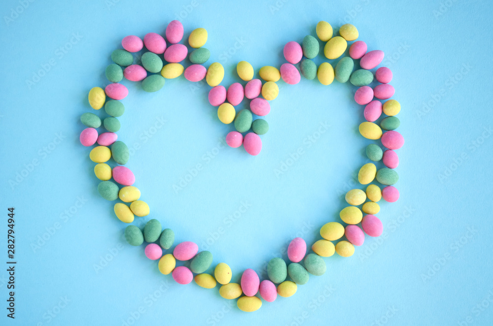 Colored sweets, peanut covered with glaze on blue background composition, heart shape, frame. Colored sweets, peanut covered with glaze on blue background composition, heart shape, frame.