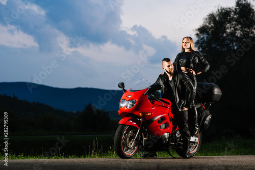 Cool biker couple in leather jackets sitting on red sports bike outdoors