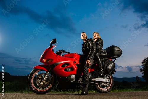 Cool biker couple in leather jackets sitting on red sports bike outdoors