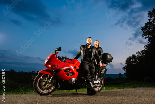 Cool biker couple in leather jackets sitting on red sports bike outdoors
