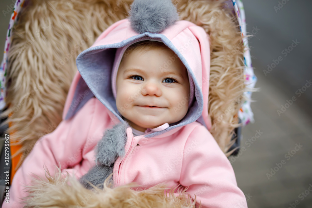 Cute little beautiful baby girl sitting in the pram or stroller on autumn  day. Happy smiling