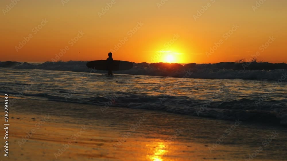 female surfer entering ocean to surf with sunrise female surfer entering ocean to surf with sunrise