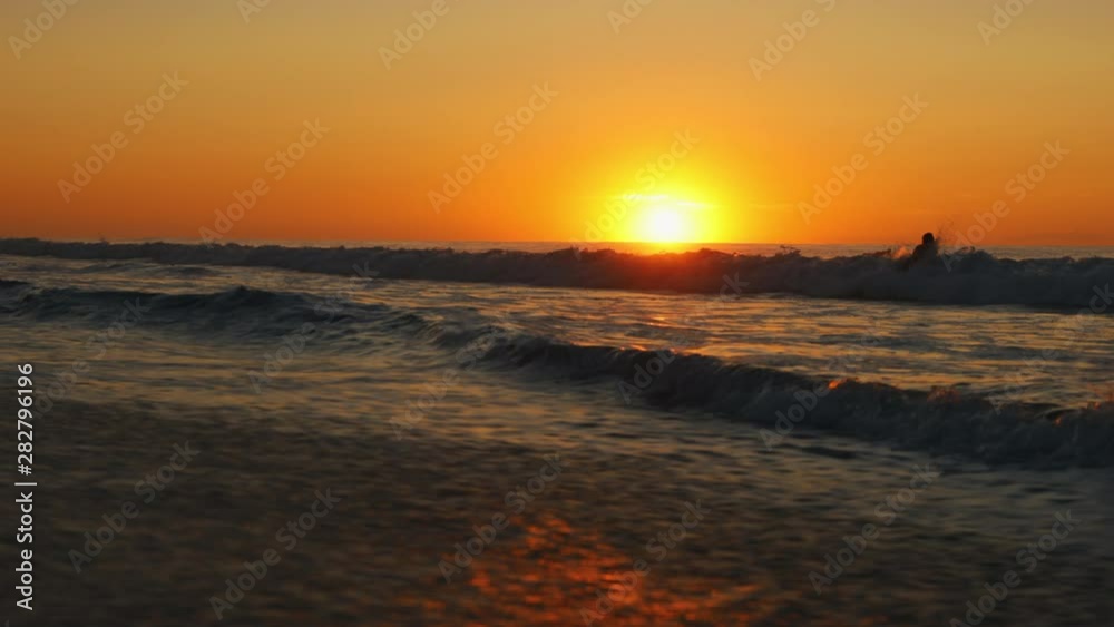 Female Surfer getting ready to surf during sunrise walking into ocean from beach with surfboard Female Surfer getting ready to surf during sunrise walking into ocean from beach with surfboard
