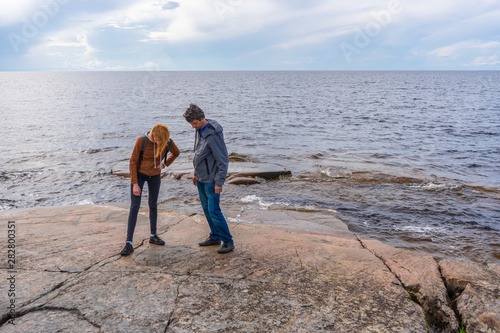 Foto Middle aged man and young lady walking on northern lake shore in summer day