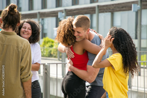 Happy Caucasian guy cuddling Afro American girl. Close interracial friends meeting on outdoor building terrace, hugging and greeting each other. Meeting and joy concept