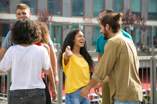 Multiethnic group of friends meeting and hugging outside. Man and woman standing on outdoor building terrace, embracing and greeting each other. Happy meeting concept