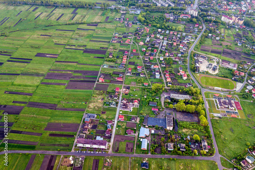 Rural landscape on spring or summer day. Aerial view of green and plowed fields, village or town house roofs and roads on sunny dawn. Drone photography.