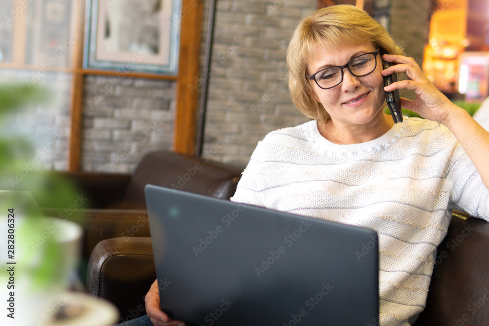 A middle-aged woman with a laptop works in a cafe in the office, she is a freelancer. A woman sits at a table with a Cup of herbal tea. She is talking on the phone. A middle-aged woman with a laptop works in a cafe in the office, she is a freelancer. A woman sits at a table with a Cup of herbal tea. She is talking on the phone.