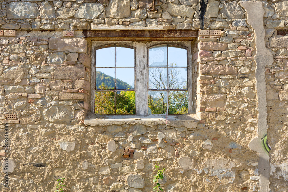 Vieille fenêtre sur un mur en vieilles pierres donnant sur un jardin