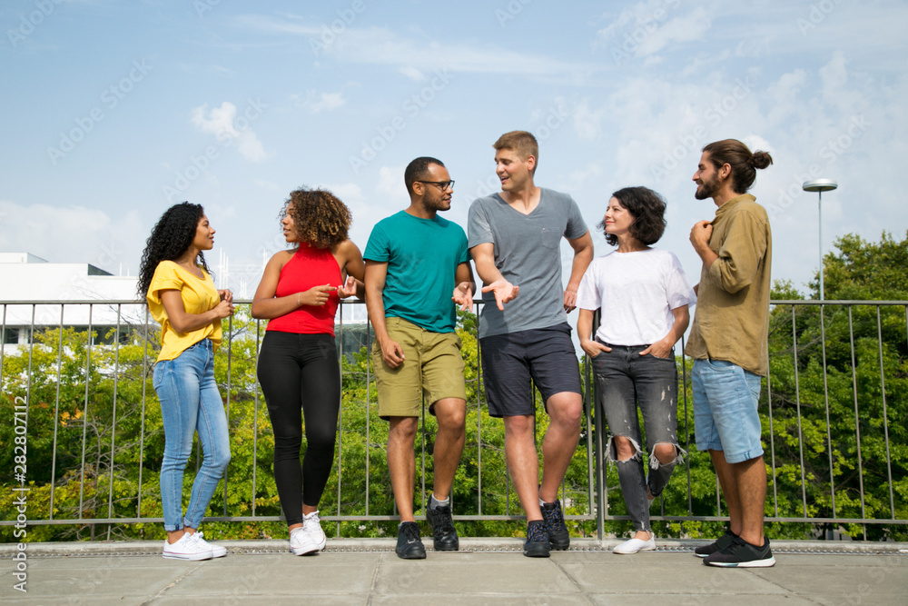 Multiethnic team of friends chatting on bridge. Mix raced group of young people standing on bridge outdoors, talking, listening, gesturing. Team of friends concept Multiethnic team of friends chatting on bridge. Mix raced group of young people standing on bridge outdoors, talking, listening, gesturing. Team of friends concept