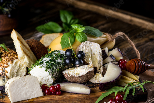 Cheese appetizer selection. Red currant, honey, basil, grapes and nuts on rustic wooden board over wooden concrete backdrop, top view. Belper Knolle, goat cheese, Scamorza. Cheese board, cheese plate. photo