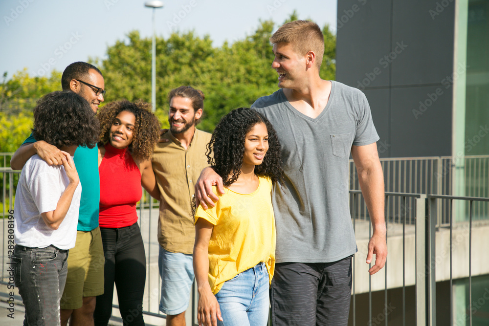 Happy mix raced couple enjoying meeting with friends outside. Multiethnic group of people walking outdoors, hugging each other, talking and laughing. Friendship and love concept