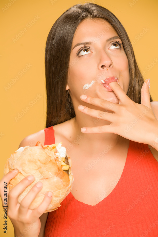 Young greedy woman eating a burger on yellow background Young greedy woman eating a burger on yellow background