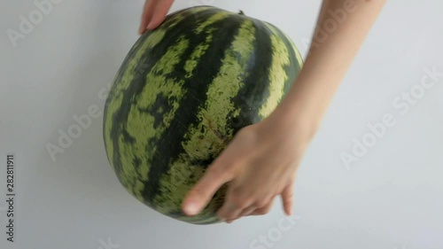 Female hands rotating whole big green striped watermelon on white table. Overhead shot