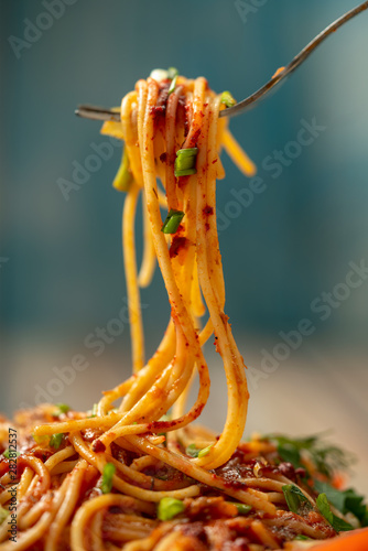 plate of pasta seasoned with herbs, tomatoes and sauce on a wooden table close-up, fork with long pasta and sauce, share menu restaurant and cafe