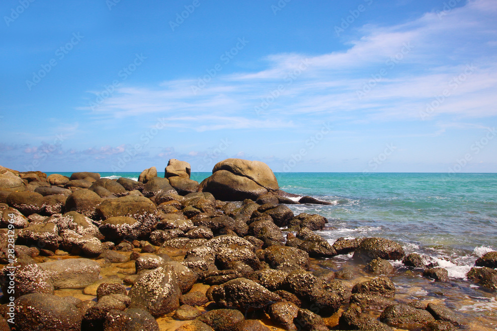 Boulders, the surf, and the blue sky over the sea, Karon sandy beach, Thailand