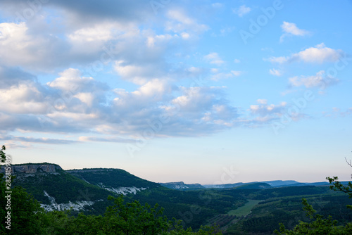 View of the gorge with growing green trees and white stone  from the top in the light of the setting sun  with clouds in the sky.