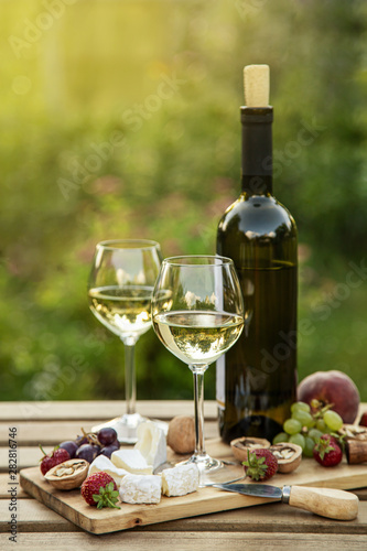 Two glasses of white wine   cheese  fruits. Romantic outdoor dinner in a garden   selective focus  toned