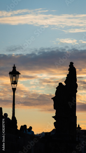 Silhouette of statue on Charles Bridge in Prague  at sunset with cloudy sky. Medieval Gothic bridge  finished in the 15th century  crossing the Vltava River