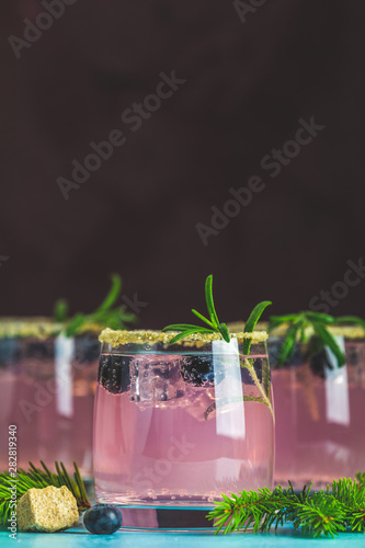 Fresh blueberry cocktail with rosemary and ice in glasses with decorate brown sugar on turquoise surface and black background. Christmas and New Year holiday welcome drink.