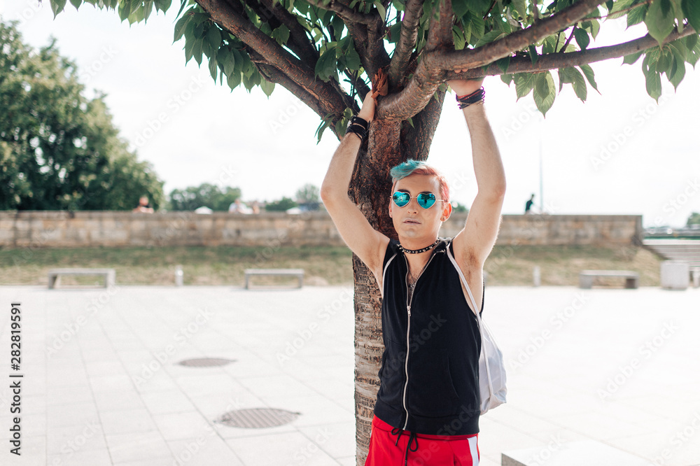 Homosexual transgender gay man posing near tree at city square