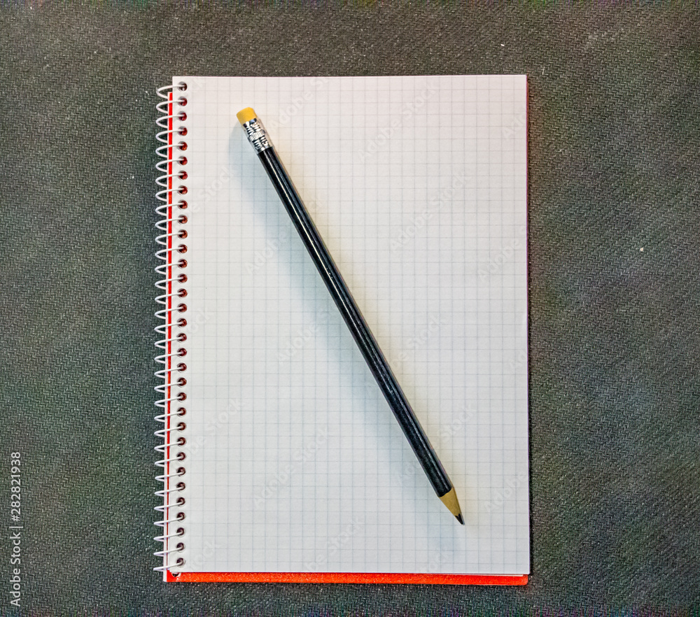 Design concept - top view of a red and gray spiral notebook and black pencil collection on black background for layout.. Design concept - top view of a red and gray spiral notebook and black pencil collection on black background for layout..