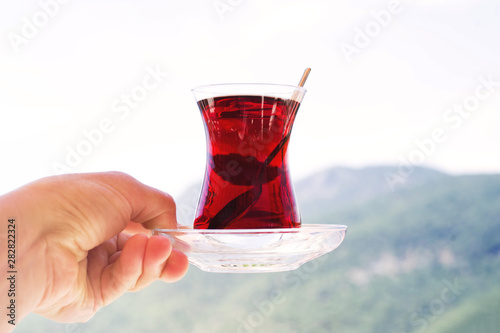 Turkish tea in a traditional glass (tulip) in hand against the background of mountains