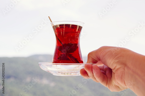 Turkish tea in a traditional glass (tulip) in hand against the background of mountains