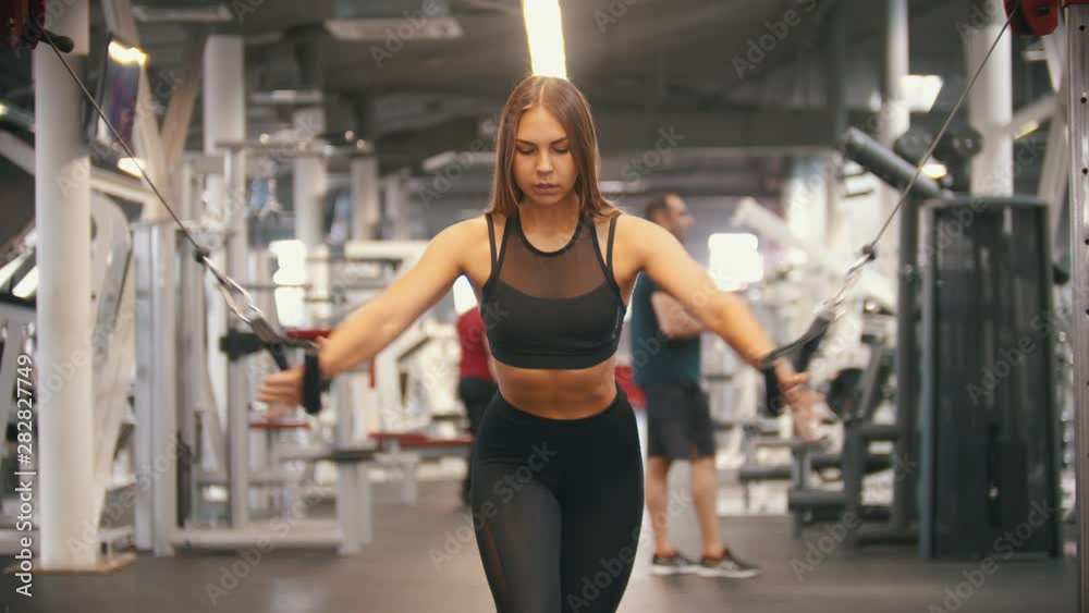 An athlete woman training in the gym - pulling the handles - training hands An athlete woman training in the gym - pulling the handles - training hands