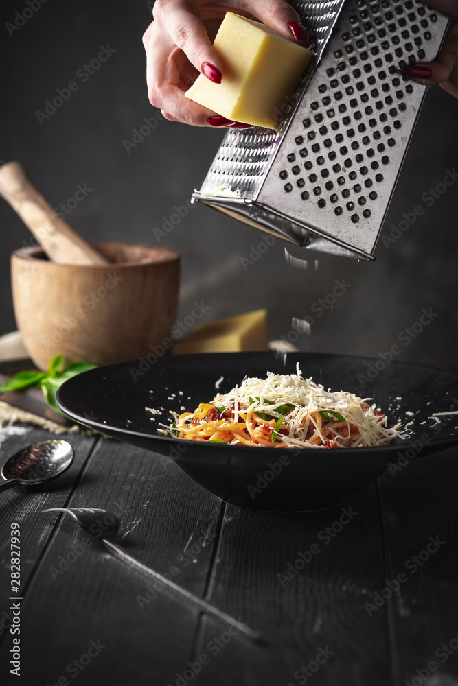 Φωτογραφία Hands grated Parmesan cheese in spaghetti Bolognese pasta with dried tomatoes and sauce in a black plate on a black wooden background