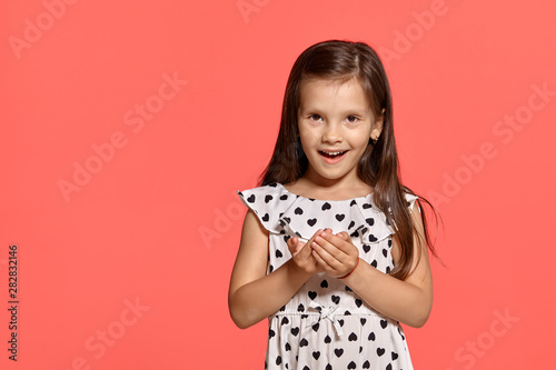 Close-up studio shot of beautiful brunette little girl posing against a pink background.