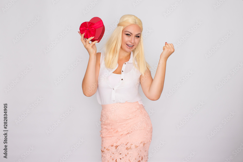Portrait of a young blonde woman in light-colored clothes. Holding a heart shaped gift box. Portrait of a young blonde woman in light-colored clothes. Holding a heart shaped gift box.