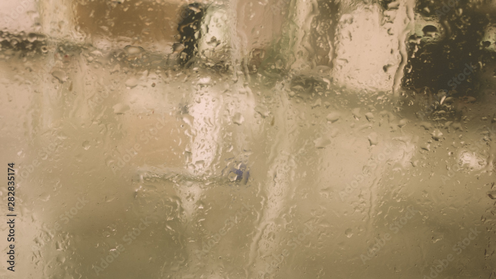 Fototapeta premium Rain Drops On Surface of wet Window Glass pane In Rainy Season. Abstract background. Natural Pattern of raindrops isolated from blurry city outdoor in a cloudy environment.