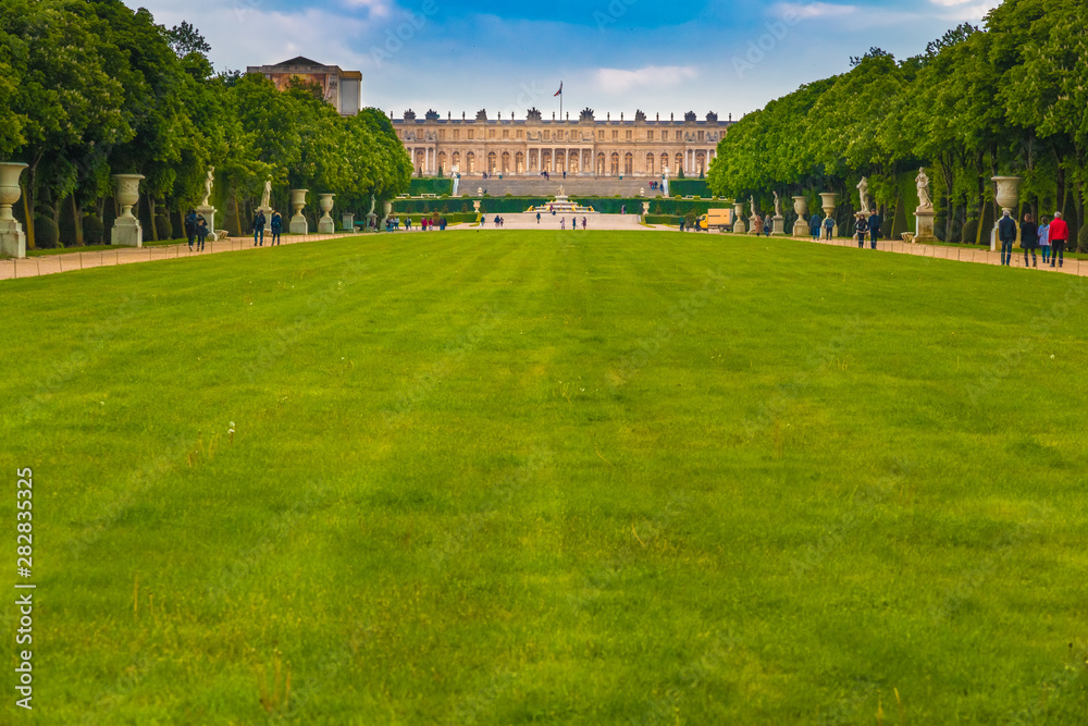Nice panoramic landscape view of the garden façade of the famous Palace of Versailles from the large lawn or green carpet (Tapis Vert) between the alleyway in the classic French formal garden. 