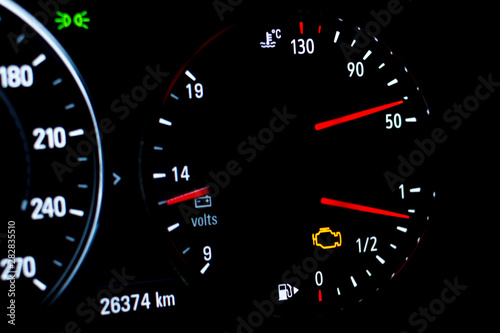 Selective focus of malfunction check engine warning light on car dashboard. Side view of modern car instrument panel with odometer, car water temperature, car voltmeter and fuel gauge.