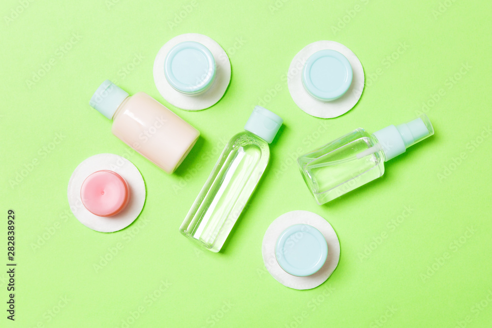 Group of small bottles for travelling on green background. Copy space for your ideas. Flat lay composition of cosmetic products. Top view of cream containers with cotton pads Group of small bottles for travelling on green background. Copy space for your ideas. Flat lay composition of cosmetic products. Top view of cream containers with cotton pads