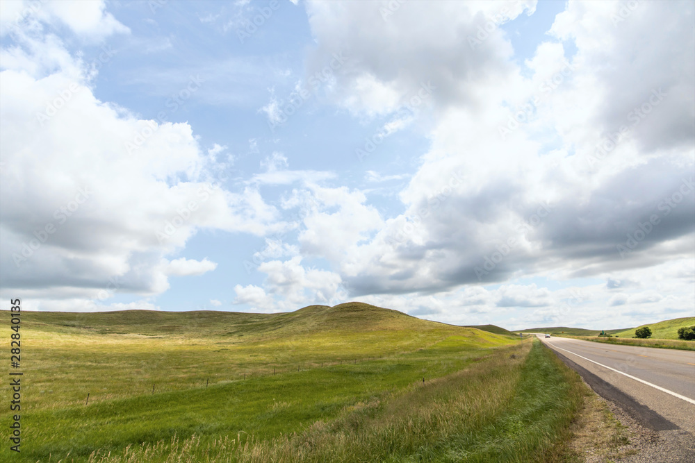 a long dirt road in rural North Dakota with a bright blue sky with clouds in the horizon